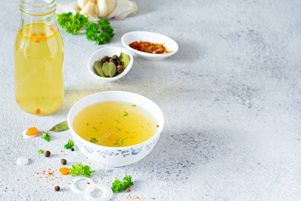 Homemade chicken (bone) broth/bouillon with vegetables, spices and herbs in a bowl (cup) on a light background. Natural collagen of animal origin. Liquid broth from meat, fish, vegetables.