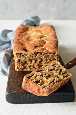 Gri arka planda et ve mantarlı gözleme turtası. Ekmek şeklinde krep. Slav mutfağı. Gri arka planda etli ve mantarlı gözleme turtası, kopyalama alanı. Shrovetide Maslenitsa