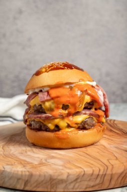 Duble hamburger. Çedar peyniri, karamelize soğan, biftek ve özel sosla. Servis masasında iki köfteli hamburger. Kapat.