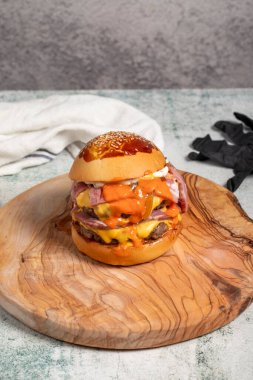 Duble hamburger. Çedar peyniri, karamelize soğan, biftek ve özel sosla. Servis masasında iki köfteli hamburger.
