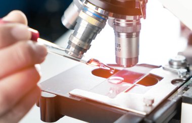 Genç Asyalı adam ve beyaz mikroskop laboratuarında test için kırmızı sıvı ve damlatıcıyla. Bilim laboratuarında teknisyenlerin sürgülü camlara kırmızı su damlatması..