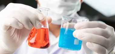 Kimyager çocuk, biber bardağındaki mavi sıvıyı ve Erlenmeyer kimyasını biyokimyasal deneydeki kırmızı sıvıyla karşılaştırıyor. Çözüm karşılaştırma kavramı.