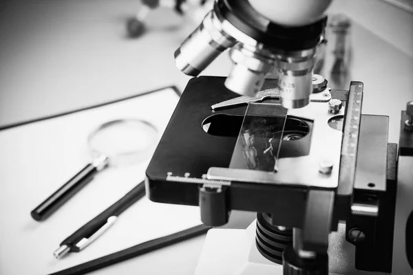 Close up of old vintage of microscope with metal lens, science equipment, pen, pencil and magnifying glass at at laboratory research desk.