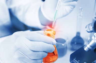 Genç Asyalı adamın elleri ve laboratuarda test için kırmızı sıvı ve damlatıcıyla birlikte beyaz mikroskop. Bilim laboratuarında teknisyenlerin sürgülü camlara kırmızı su damlatması..