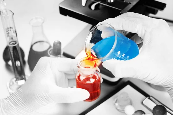 Chemist student boy pouring blue liquid in beger glass to erlenmeyer flask chemistry with red liquid on biochemical experiment. Mix water in laboratory.