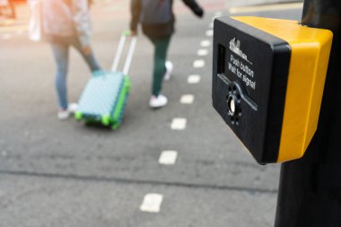 Londra 'daki yaya geçidi sinyali için sarı metal yaya geçidi düğmesini kapatın trafik kuralları için Uk. İki kişi yaya çapraz düğmesi kullanarak caddeyi geçiyor..