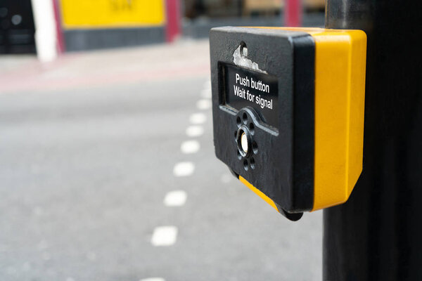 Close up of yellow metal crosswalk button for pedestrian crossing signal in London, UK for traffic rules. Classic pedestrian cross button in Europe.