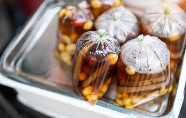 A plastic cup and plastic bag of cold assorted beans, lotus roots, ginkgo, longan and sweet syrup in street food shop in asian for healthy and refresh know as Sweet Taothueng in Thailand.