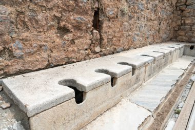 Türkiye 'nin Selcuk İzmir kentindeki Efes' teki görkemli antik harabelerde çok koltuklu tuvalet mermeri taşı ve kaya bulunuyor. Tarihi Antik Yunan tuvalet sistemi taşı.