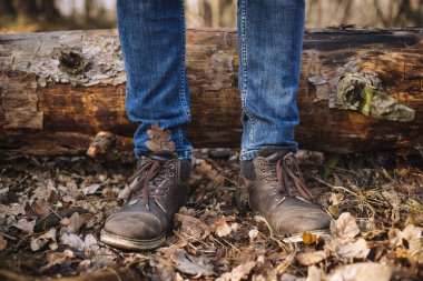 Eski deri botlar ve yerde kurumuş yapraklarla dikilen kot pantolon giymiş insan bacakları fotoğrafı.