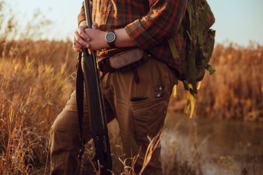Erkek avcıların elleri, ellerinde av tüfeği, gün batımında, ördeği bekliyorlar.