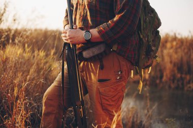 Erkek avcıların elleri, ellerinde av tüfeği, gün batımında, ördeği bekliyorlar.
