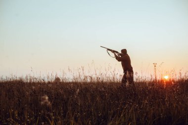 Avcı 'nın mavi gökyüzü ve kırmızı güneşli karanlık silueti - seçici odaklı fotoğraf