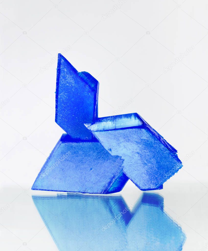 Blue crystals of copper sulfate on mirror surface, white background, blue vitriol, copper sulphate