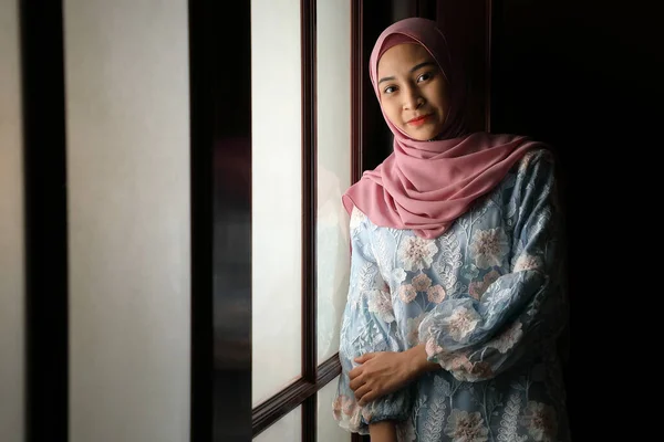 年轻的亚裔马来人穆斯林妇女头戴头巾 头戴白菊 在家里的前窗 心情轻盈 脸色阴郁 背景平静 心平气和 心平气和 无忧无虑 幸福无比 — 图库照片