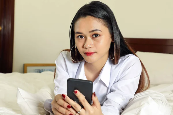 Young beautiful modern Malay woman sit on bed work study read write in bedroom laptop tab book smile look at camera