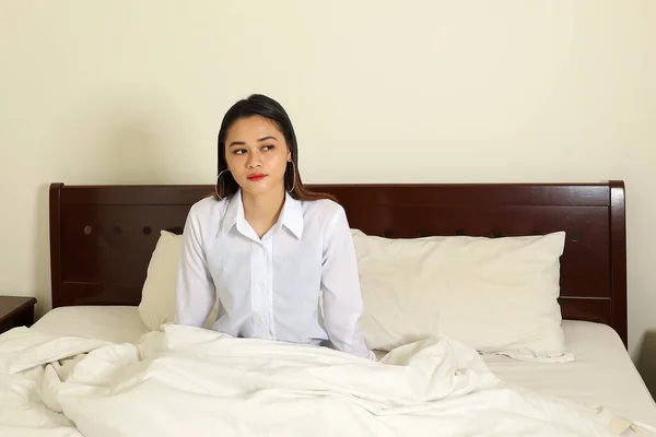 Young beautiful modern Malay woman sit on bed work study read write in bedroom laptop tab book smile look at camera