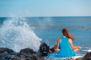 Kadın pratiği Yoga cliff, fırtınalı okyanus üzerinde. Arkadan görünüm. Mavi gökyüzü. Sağlıklı yaşam konsepti.