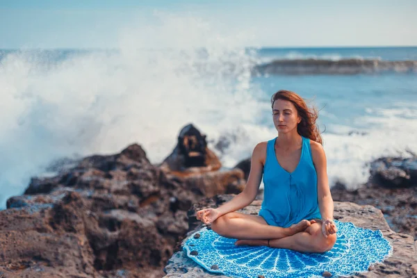 Junge Frau praktiziert Yoga auf einer Klippe, sie meditiert in Lotusposition. — Stockfoto