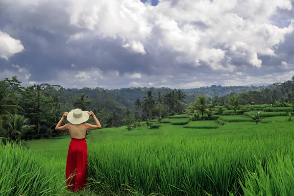 Hermosa mujer joven en vestido rojo toque sombrero de paja. Chica caminar en la ladera típica asiática con cultivo de arroz, forma de montaña verde cascada campos de arroz terrazas de arrozales. Ubud, Bali, Indonesia . —  Fotos de Stock