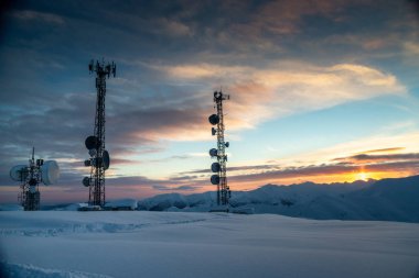 İletişim kulesi antenler ve çanak antenler, günbatımında bir kış dağ manzarası arka plan ile. Gudauri, Gürcistan