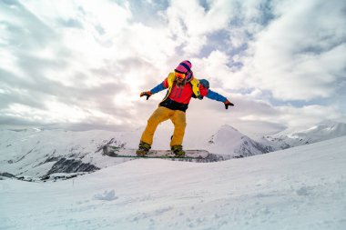 Güneşli bir günde yüksek dağlara atlayan snowboardcu..