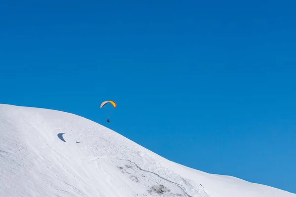 晴れた冬の日にスキーリゾートの上に雪の山でパラグライダー。コーカサス山脈ジョージア州, 地域グダウリ. — ストック写真