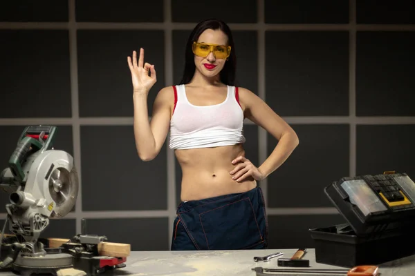 Donna in maschera gialla, mostrando gesto OK, lavorando in falegnameria — Foto Stock