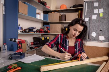 Bir cetvel ile çalışan ve kumaş atölyesinde masada ahşap üzerinde işaretleri yapma çalışkan odaklı profesyonel ciddi marangoz kadın yakından görünümü.