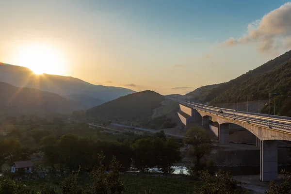 Güzel asfalt yol. Yüksek kayalar, dağ yolu mükemmel bir asfalt, ağaçlar ve inanılmaz güneşli bulutlu gökyüzü yaz aylarında gün batımında, renkli yatay. Arka plan seyahat. Dağlar, otoyol. Yol