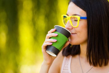 Güzel kız poz yeşil bokeh arka plan üzerinde elinde kahve için. Kağıt bardak kahve yeşil bokeh arka plan üzerinde kızla.