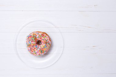 Şeffaf cam plaka üzerinde beyaz ahşap masa, üstten görünüm krem tepesi ile sırlı pembe çörek.