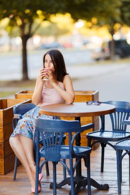 Bir yaz teras bir Cafe de oturup bir sıcak kahve ile güzel bir gülümseyen mutlu Bayan portresi. Genç bir kız oturuyor ve bir restoran masada kahve içme.
