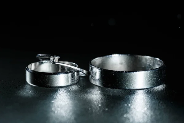 Beautiful wedding silver rings on dark wet glass with water drops.