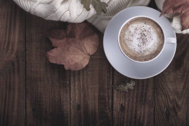 Sıcak kahve kapuçino, battaniye ve sonbahar yaprakları eski ahşap zemin üzerinde. Vintage tonlama. Mevsimsel rahatla kavramı