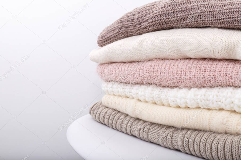 Stack of cozy knitted sweaters or blankets pastel trending colors on white modern chair against the wall