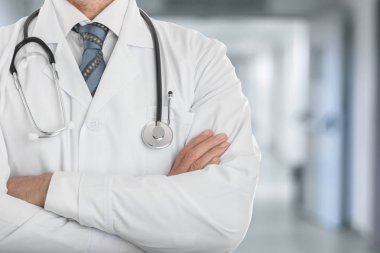 Klinikte çapraz elle bir stetoskop konumu olan beyaz montlu erkek doktor
