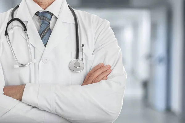 Klinikte çapraz elle bir stetoskop konumu olan beyaz montlu erkek doktor
