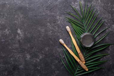 Koyu gri arka planda doğal bambu diş fırçaları ve siyah diş tozu, sıfır atık ürün, doğal ağız temizliği, kopyalama alanı
