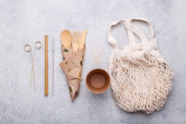 Sıfır atık bambu sofra takımı, çevre dostu kağıt bardak ve peçete, saman, çanta, doğal taştan arka planda ahşap çatal bıçak takımı. Üst görünüm kopyalama boşluğu
