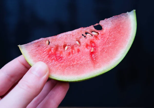A slice of juicy fresh mini watermelon in a female hand on a dark background. — Stock Photo, Image