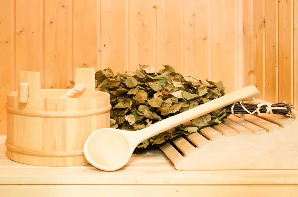 A wooden bucket, a birch broom and other accessories in a finnish classic sauna or russian bath. Free space on a wooden background