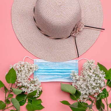 Tıbbi maske, yaz, ödenmiş şapka, pembe arka planda leylak. Düz konsept: Tatilde koronavirüsten korunuruz