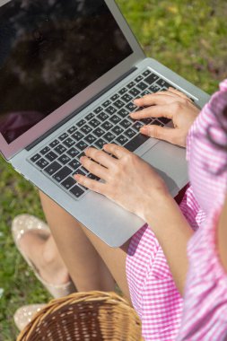 Açık havada dizüstü bilgisayar üzerinde çalışıyorum. Kesilmiş görüntü, dizüstü bilgisayarda çalışan genç bir kız, parkta oturuyor. Fotoğraf: