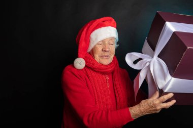 Sly, cüce şapkalı mutlu büyükannenin elinde yeni yıl hediyesi var. Siyah arka plan fotoğraf stüdyosunda. Mutlu yıllar 2021.