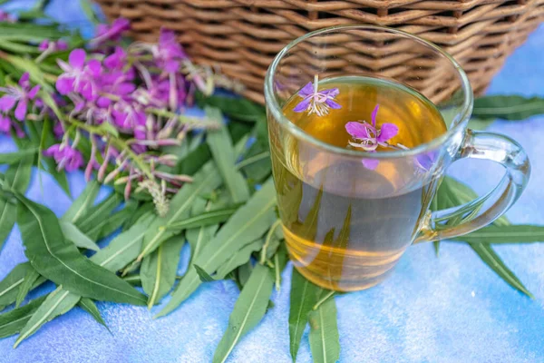 Traditional Russian herbal drink Ivan tea in a transparent cup. Close-up, leaves of Ivan tea, fireweed, wicker basket background. — Stock Photo, Image
