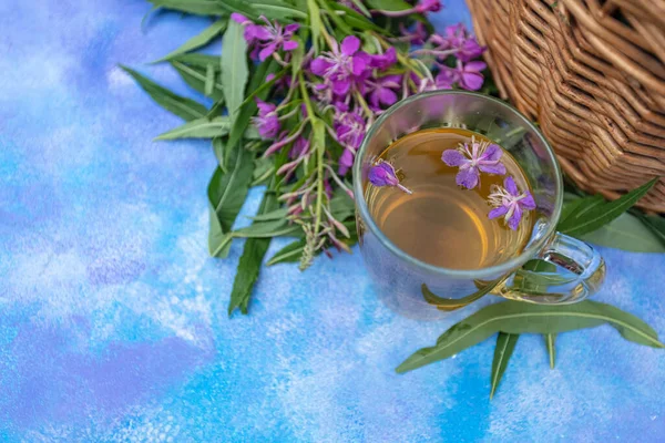Hagyományos orosz gyógynövény ital Ivan tea átlátszó csészében. Közelkép, levelek Ivan tea, tűzfű, fonott kosár háttér. — Stock Fotó