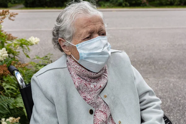 Tekerlekli sandalyedeki tıbbi maskeli yaşlı kadın yürüyüşe çıktı. Coronavirus koruması