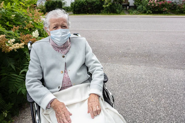 Tekerlekli sandalyedeki tıbbi maskeli yaşlı kadın yürüyüşe çıktı. Coronavirus koruması