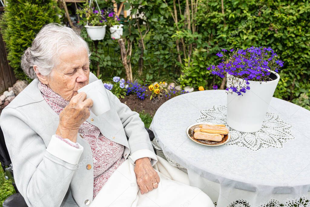 Old woman in a wheelchair drinking tea on the terrace